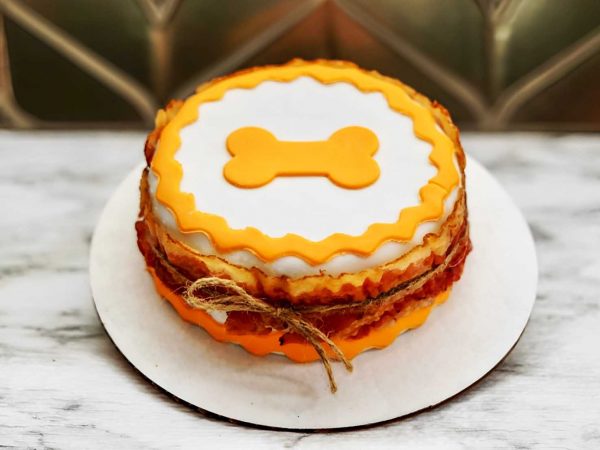 A layered round cake with white and orange icing, decorated with a bone shape on top