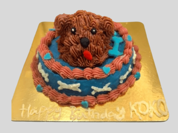 A round two-layer dog cake with a 3D sculpted dog head on top, decorated with pink and blue frosting and small hearts.