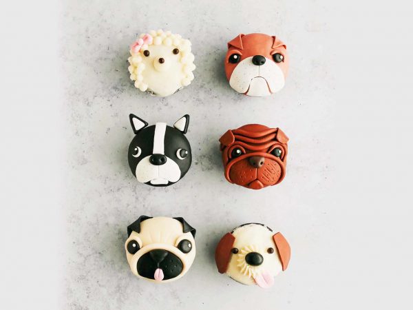 Six cupcakes decorated with dog face designs with various breeds,