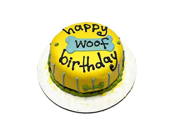 Bright yellow dog birthday cake with “Happy Woof Birthday” written with icing