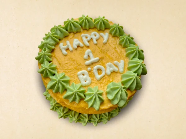 Round dog birthday cake with yellow frosting and green star-shaped patterns
