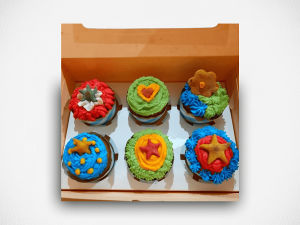 Colorful dog-friendly cupcakes with fresh frosting and star-shaped treats, arranged in a cardboard box.