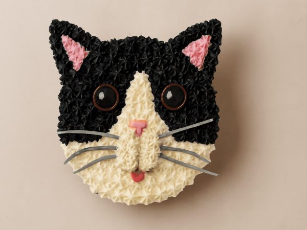 Black and white cat-face shaped cake with pink ears and tongue